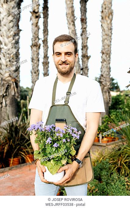 Portrait of a smiling worker in a garden center holding a lilac plant