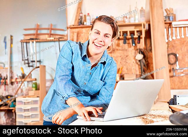 Glückliche junge Frau als Tischler Azubi am Laptop Computer online in der Werkstatt