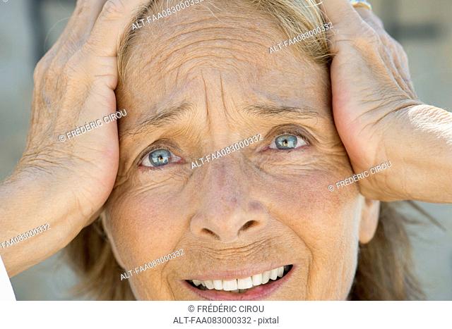 Senior woman holding head, distressed expression on face