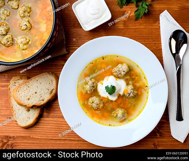 vegetable and meatball soup on wooden table in white plate