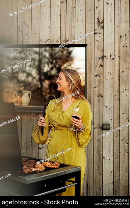 Smiling woman holding wine glass and barbecuing meat