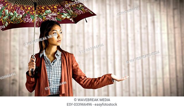Millennial woman with patterned umbrella and hand out against blurry wood panel