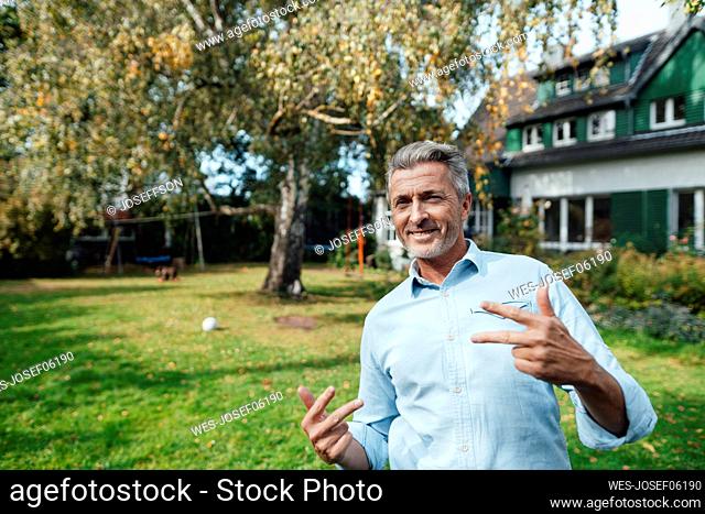 Smiling man gesturing hand sign at backyard