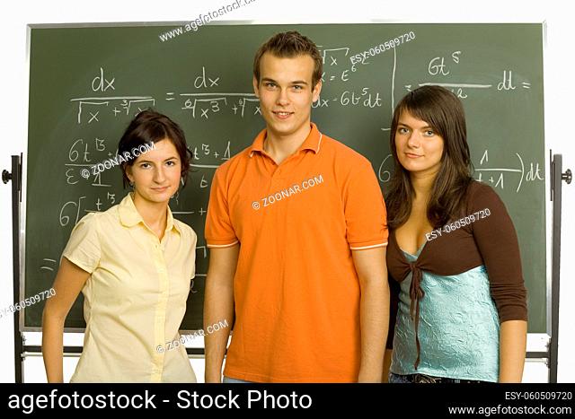 Small group of teenagers standing in front of blackboard. Smiling and looking at camera. Front view