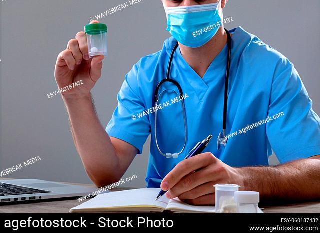 Caucasian male doctor wearing face mask holding box of pills