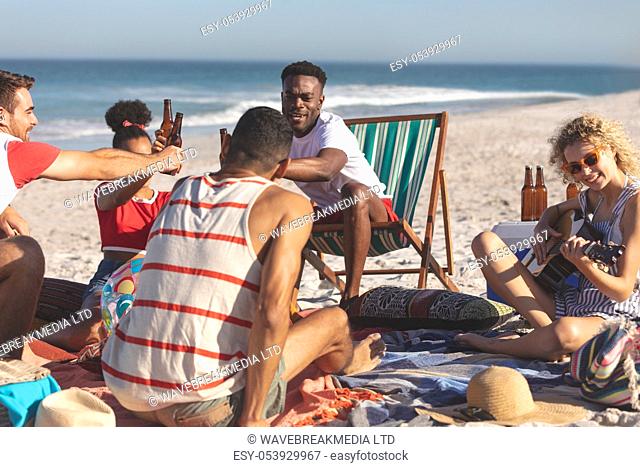 Front view of group of happy diverse friends toasting glasses of beer on the beach