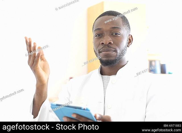 Young black doctor with smock and tablet explaining in the surgery, Freiburg, Baden-Württemberg, Germany, Europe