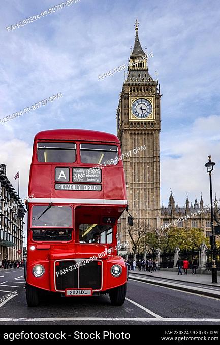 30 October 2022, Great Britain, London: A red double-decker bus (double-decker) drives along in front of the Elizabeth Tower, where the bell Big Ben hangs