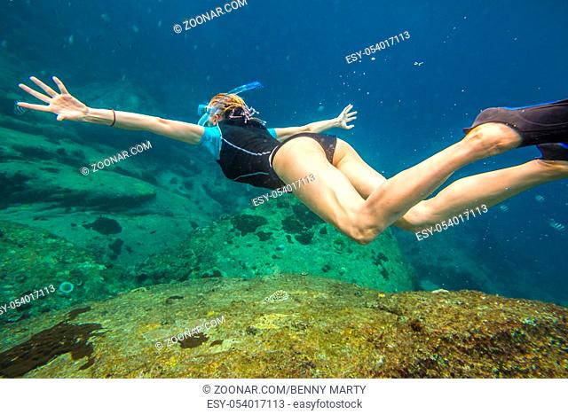 Young woman free diving in the blue waters of the popular Similan Islands in Thailand, one of the tourist attraction of the Andaman Sea