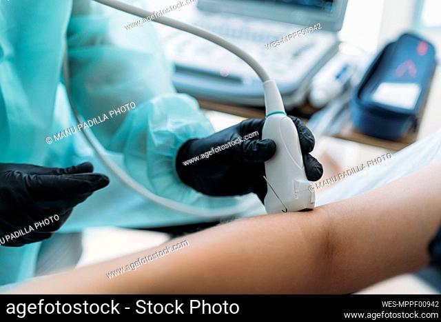 Doctor wearing protective clothes examining woman's arm with ultrasound scanner