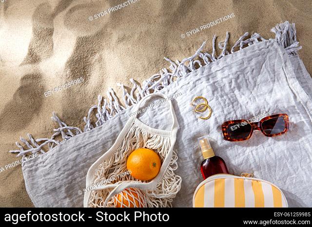 bag of oranges and sunscreen oil on beach blanket