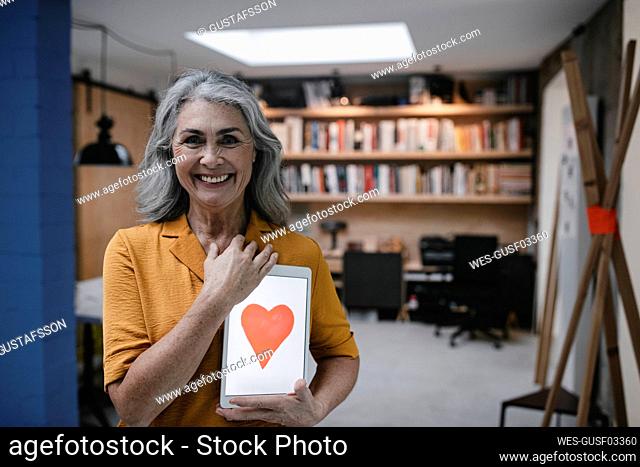 Smiling grey-haired woman holding tablet with a heart on the screen