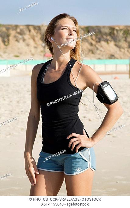 A young model in her 20's on a beach, enjoys herself while she listens to a music player attached to her arm - model release available