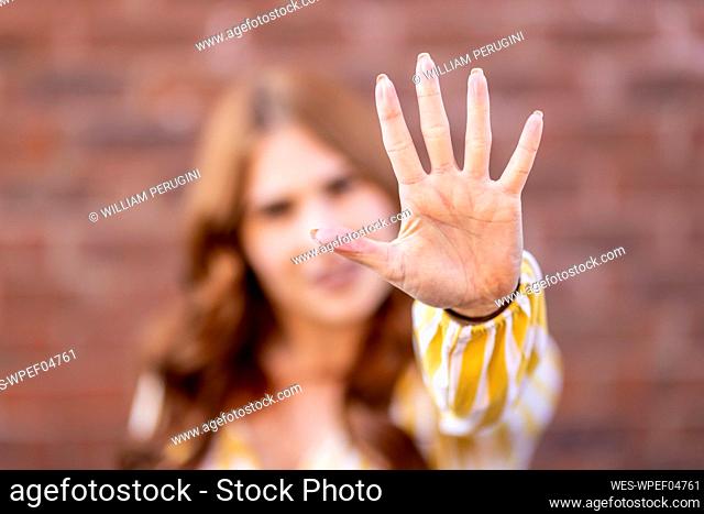 Mid adult woman gesturing stop sign against brick wall
