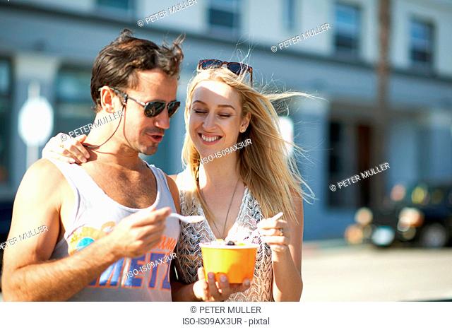 Couple strolling and sharing frozen yoghurt on sidewalk, Venice Beach, California, USA