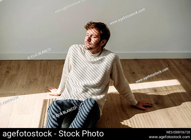 Businessman relaxing with shadow of window blinds on face sitting in office
