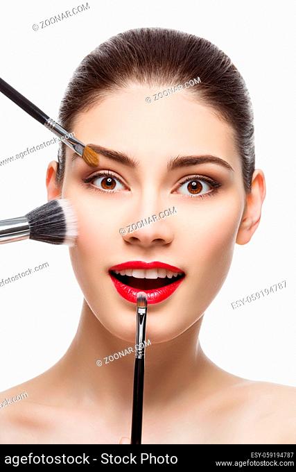 Closeup portrait of beautiful young woman with makeup brushes. Red lips. Happy expression. Isolated over white background