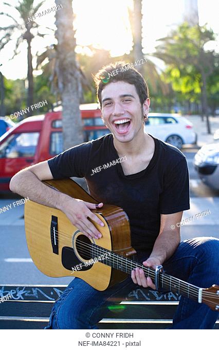 Portrait of young man playing guitar, outdoors