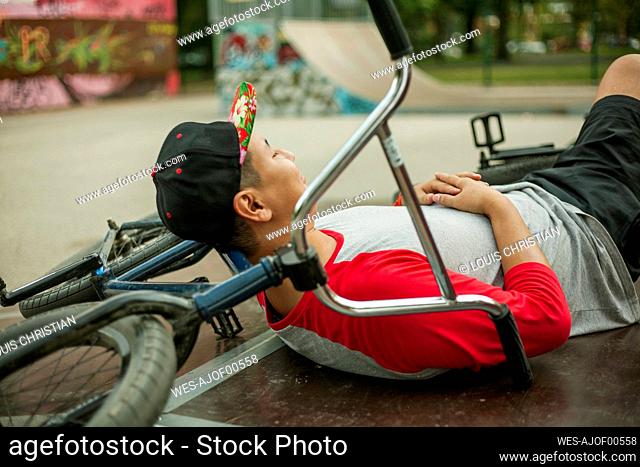 Young man resting on BMX bicycle at skateboard park