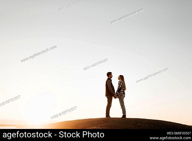 Young couple holding hands against clear sky at sunset