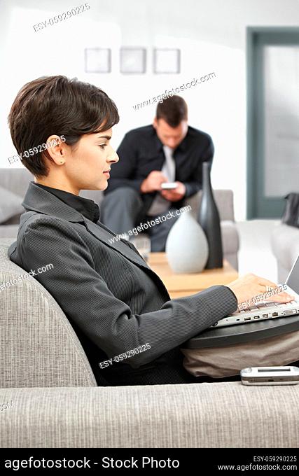 Young attractive businesswoman sitting on sofa at office lobby working with laptop computer, smiling