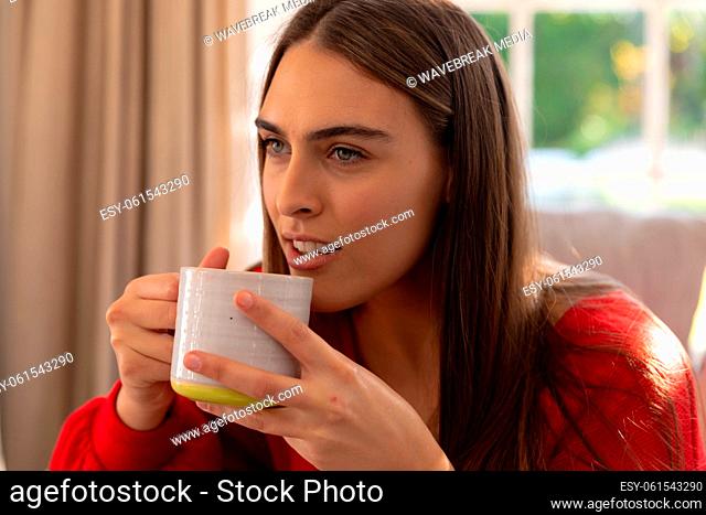 Happy caucasian woman sitting on couch drinking coffee in sunny living room