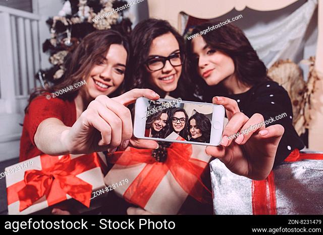 Beautiful girl photographed themselves on the phone on the background of Christmas gifts. Decorative vintage apartment