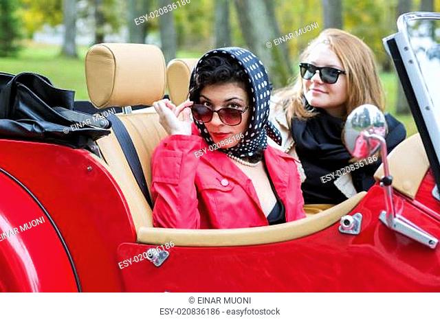 women at retro red car look satisfied