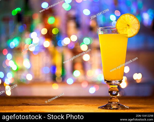 Glass of orange cocktail on a bar lights background