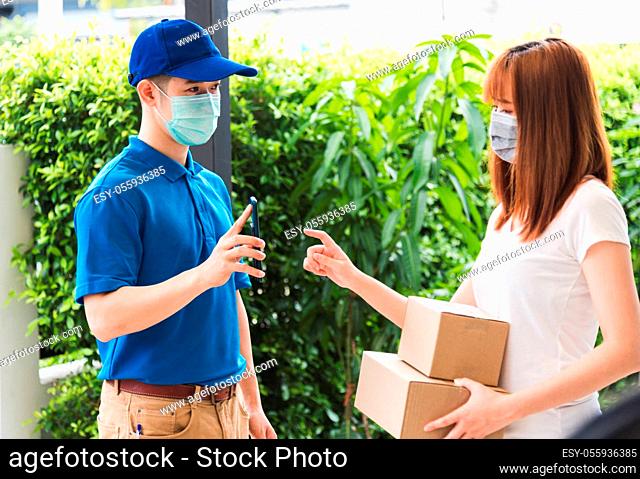 Asian delivery express courier young man giving parcel boxes to woman customer signature for receiving on mobile phone both protective face mask