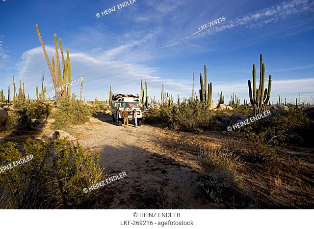 A family standing in front of a school bus amidst cactuses in the desert, Catavina, Baja California Sur, Mexico, America