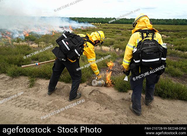 28 July 2021, Brandenburg, Brück: Members of the organisation @fire Internationaler Katastrophenschutz Deutschland e. V. set fire to an open area of heath on...
