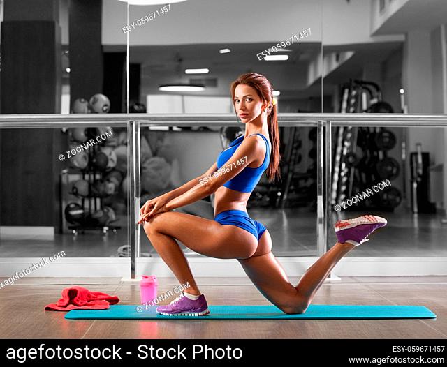 Attractive young woman is doing plank exercise while working out in gym. Beautiful slender brunette girl in blue sportswear