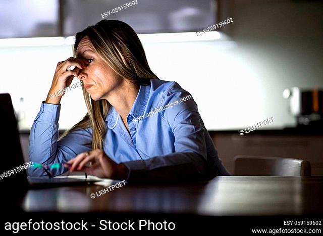 Pretty, middle-aged woman working late in the day on a laptop computer at home, running a business from home, working remotely - getting frustrated, exhausted