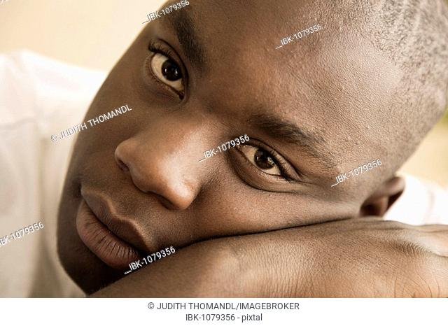 Dark-skinned, 15-year-old boy, head resting on hand, looking into camera