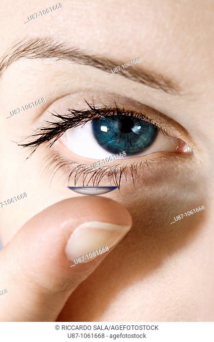 A facial close up of a young woman putting a contact lens onto his eye