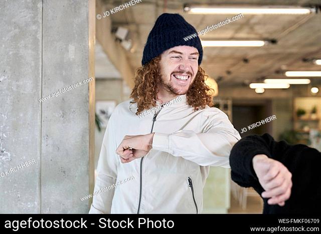Smiling hipster man doing elbow bump with female friend while standing at home