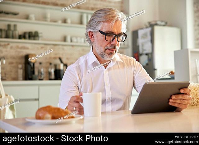 Businessman with digital tablet having coffee at office cafeteria