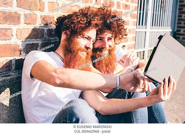 Young male hipster twins with red hair and beards browsing digital tablet on sidewalk
