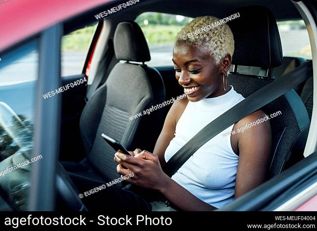 Smiling woman using mobile phone while sitting in car