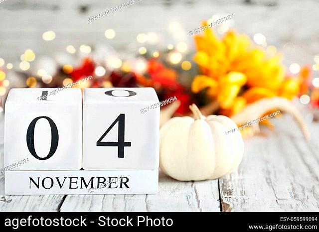 White wood calendar blocks with the date November 4th and autumn decorations over a wooden table. Selective focus with blurred background