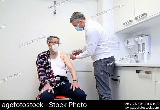 07 April 2021, Saxony-Anhalt, Schönebeck: GP Robin John (r) administers the first vaccination with the Corona vaccine Comirnaty from Biontech/Pfizer to...