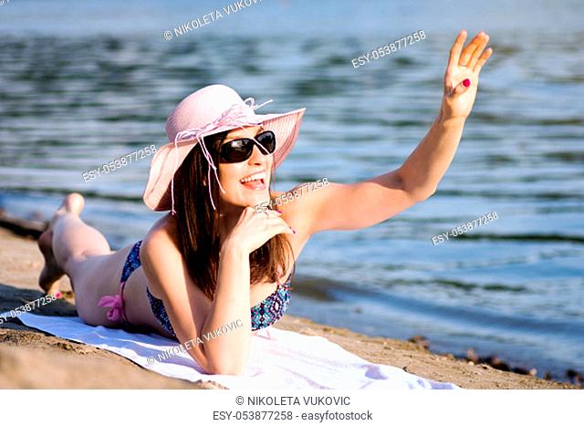 The smiling cheerful woman is greeting, saying hello and waving hand to someone on the beach at summer