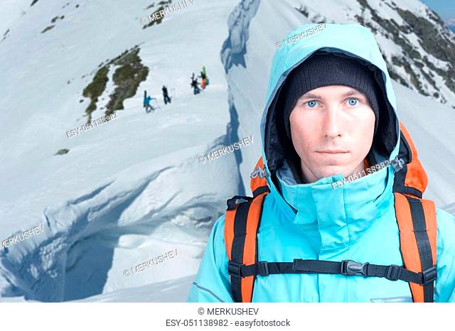 Mountaineer man stands in mountains, Snowboarders walking uphill for freeride in the background. Extreme winter sport