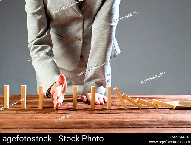 Businesswoman interrupting domino effect by stop falling wooden dominoes. Operative business solution, strategy and successful intervention