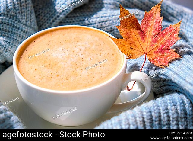 White cup of morning warming coffee on blue knitted sweater with maple yellow leaves background. Cozy home concept. Aesthetics blog lifestyle