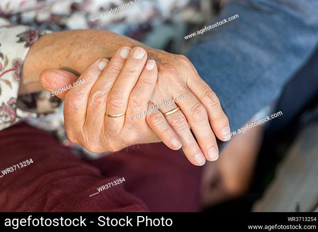 Close-up of holding hands of an 80 year old couple with wedding rings. Nahaufnahme einander haltender Hände eines 80-jähringen Ehepaars mit Eheringen