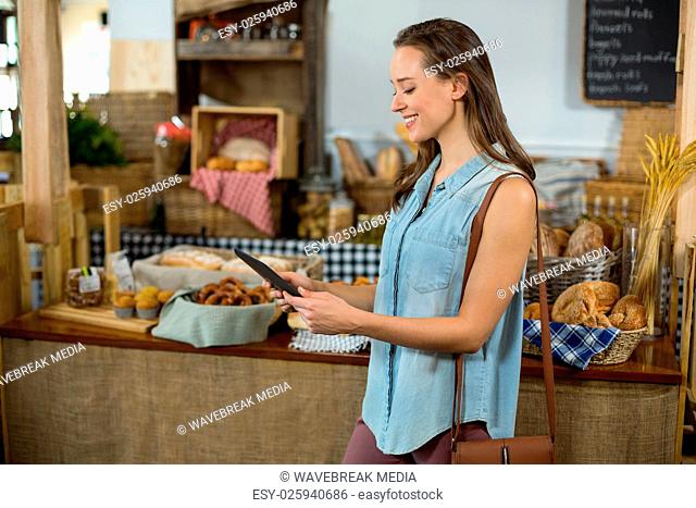 Smiling woman standing at counter using digital tablet