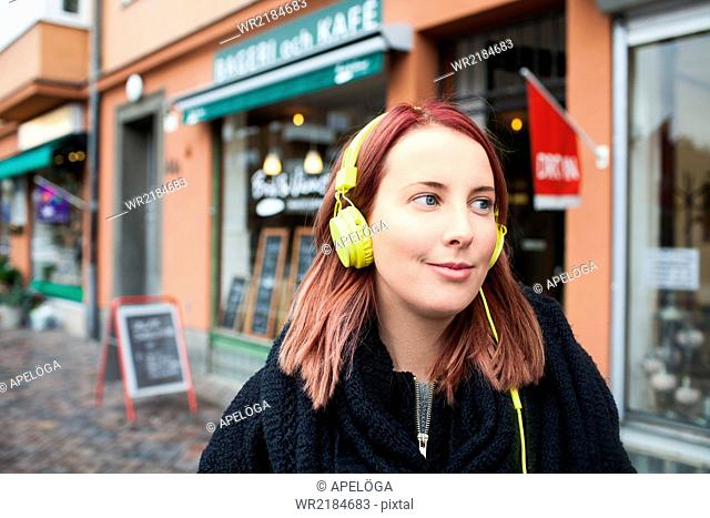 Smiling young woman listening music through headphones outside cafeteria