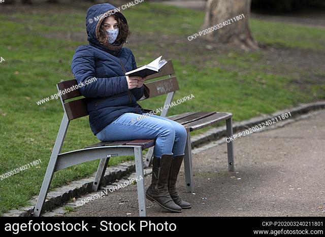 A woman with a protection face mask read a book sitting on a parrk bench in Pilsen, Czech Republic, on March 24, 2020. (CTK Photo/Miroslav Chaloupka)